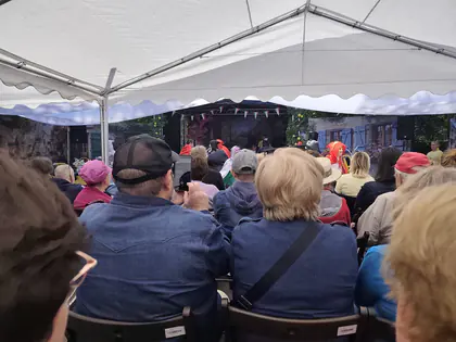 Widzowie siedzą pod namiotem przed sceną na festynie