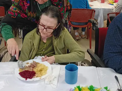 Kobieta w kolorowej chuście pomaga starszej pani w posiłku