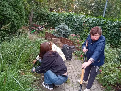 Mieszkanki grabią liście na alejce w ogrodzie