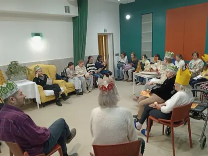 Osoby w papierowych koronach siedzą w kręgu na sali, w tle żółte fotele