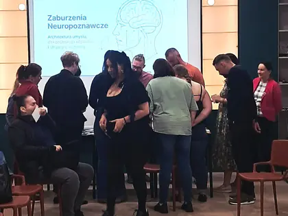 Grupa ludzi na sali, z przodu ekran ze slajdem z napisem Zaburzenia neuropoznawcze i rysunkiem głowy z zarysem mózgu