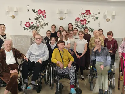 Starsze osoby, z tyłu stoi młodzież pod muralem w kolorowe kwiaty na białej ścianie